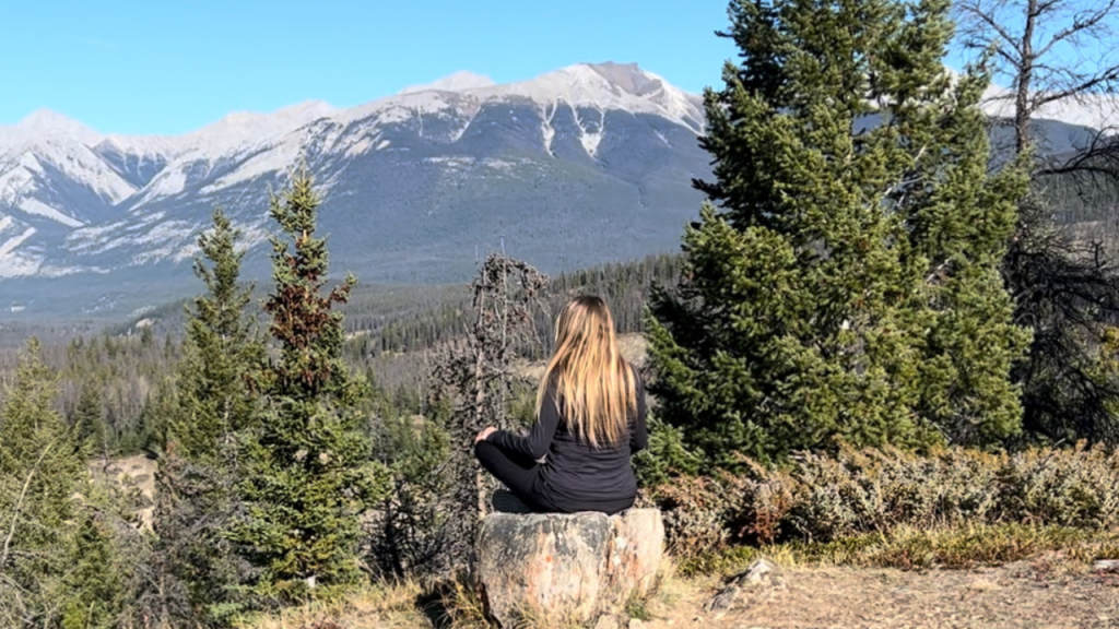 Angela V meditating on a large tree stump overlooking nature in the mountains